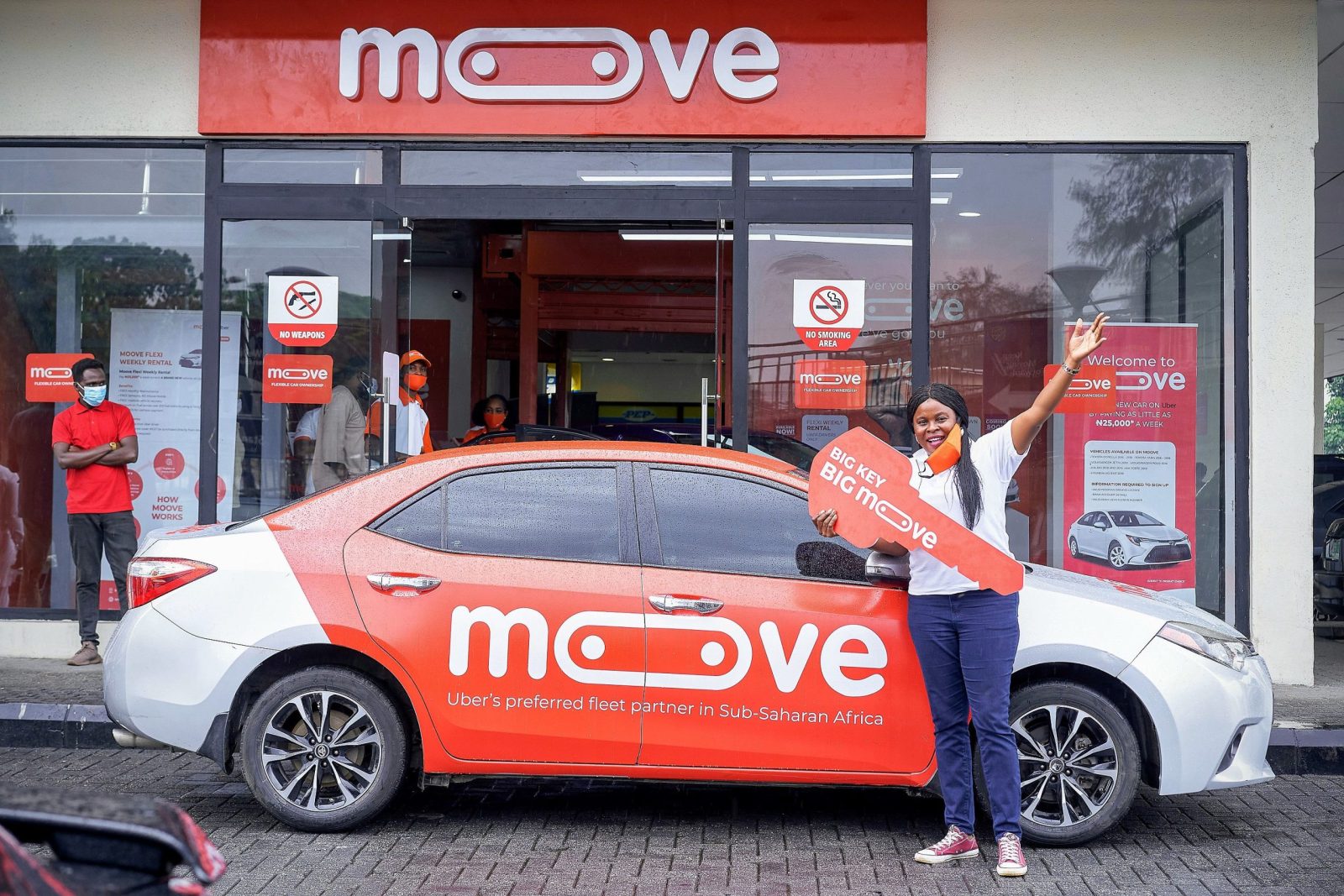A Moove-branded vehicle parked outside, with company representatives standing nearby holding an oversized key. The image represents Moove’s vehicle-financing business, which helps drivers access vehic