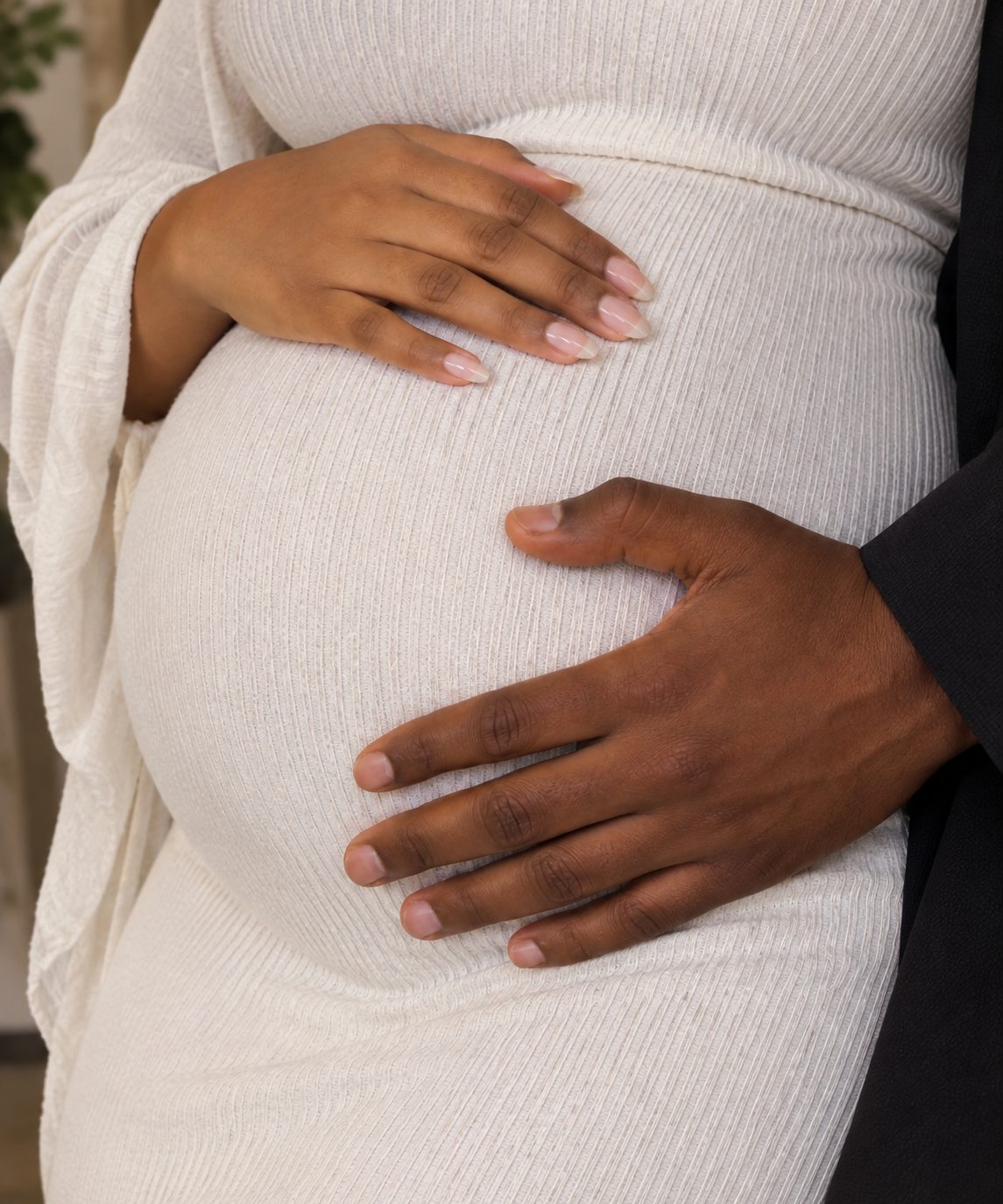Shows a woman's hand and a man's hand on a pregnant belly